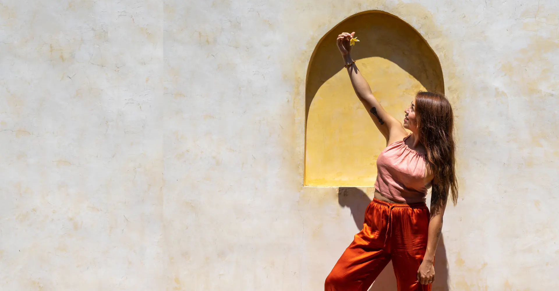 Javiera beneath a sunlit arch, holding a flower